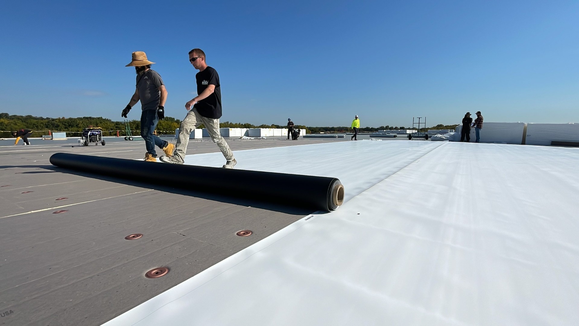 Commercial roofing installation with workers rolling out roofing material