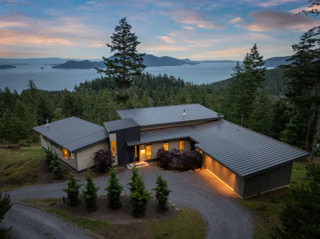 Modern mountain home with metal roof overlooking ocean and mountains at sunset