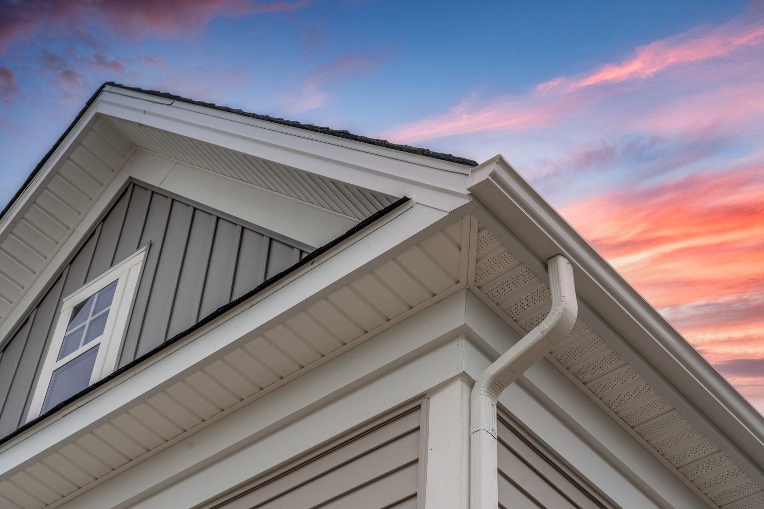 House siding, soffit and fascia with white gutters against sunset sky
