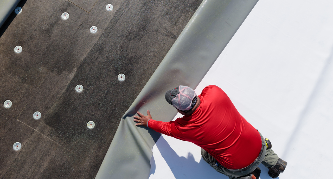Professional roofer in red shirt installing TPO membrane on commercial flat roof